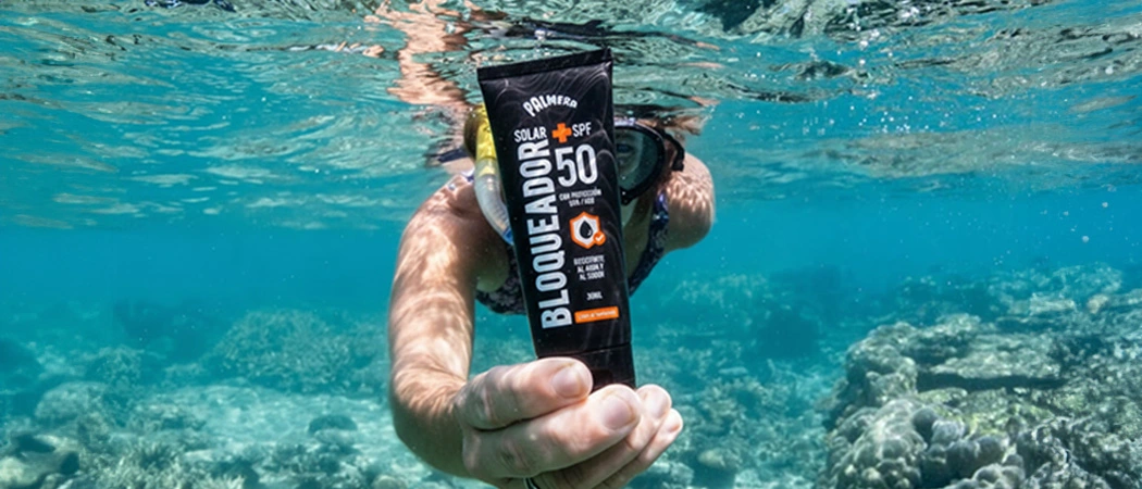 Bloqueador solar sostenido por una mano bajo el agua